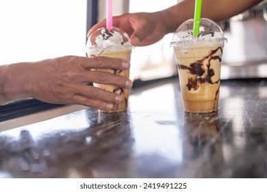 Close-up view of the hands of a barista serving two frappe to take away to a client in a food truck - Powered by Shutterstock