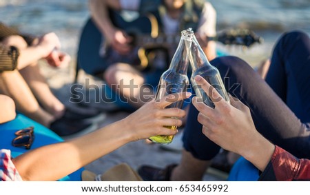 Closeup view of hands clinking glasses of beer bottles. Party on the beach with guitar