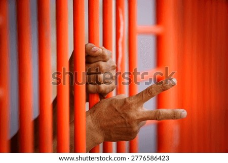 A close-up view of hands making a peace sign through bright orange prison bars, embodying the struggle for freedom and hope in confinement.