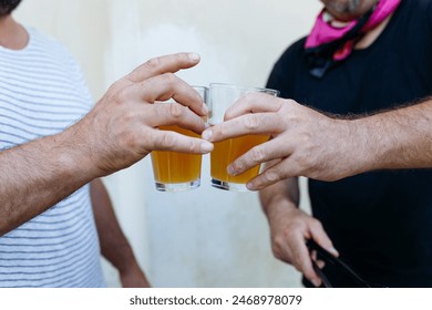 close-up view of hands of two men holding glasses of beer against yellow wall outdoors,