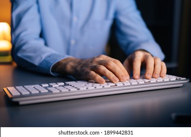 Close-up view of hands of unrecognizable man working typing on wireless keyboard computer. Male freelancer or student is working sitting on desk at home office at late night in dark room. - Powered by Shutterstock