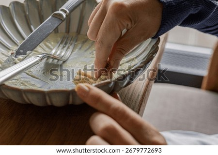 A close-up view of hands using a piece of bread to clean off remaining food on a plate for an intimate dining moment. Yummy food, leftovers, hunger concept
