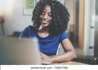 Closeup view of happy african american woman working laptop while sitting at wooden table in the living room.Horizontal.Blurred background