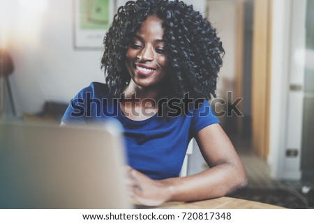 Closeup view of happy african american woman working laptop while sitting at wooden table in the living room.Horizontal.Blurred background