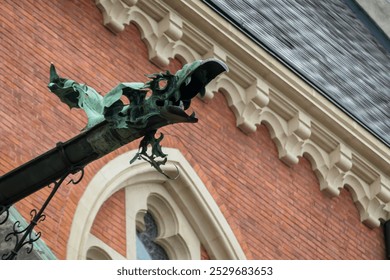 Close-up view of a historic building facade of church Herz Jesu Kirche in Graz, Styria, Austria. Large gargoyle-like sculpture of dragon, perched atop the building. Red brick exterior, ornate windows - Powered by Shutterstock