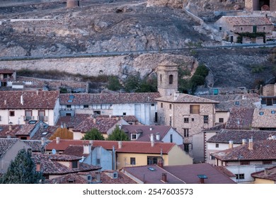 Close-up view of a historic village with stone church tower and red-tiled rooftops against a rocky hillside backdrop - Powered by Shutterstock