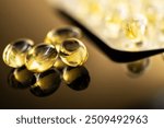 Close-up view of holden yellow transparent capsules containing vitamin D and omega-3 fish oil supplements, displayed on a reflective surface, ideal for health and wellness concepts.