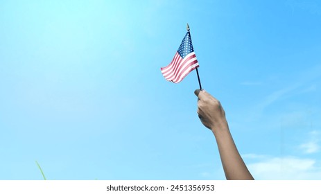 Closeup view of a human hand holding an American flag with a blue sky background. 4th of July concept - Powered by Shutterstock