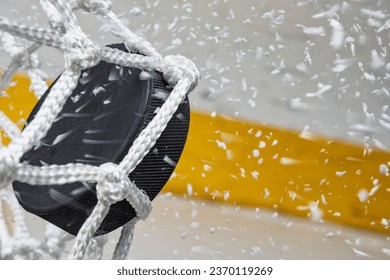 A close-up view of an Ice Hockey puck hitting the back of the goal net as shavings fly by, viewed from the side. Scoring a goal in ice hockey. - Powered by Shutterstock