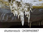 Close-up view of icicle stalactites inside a cold, dark cave in winter.