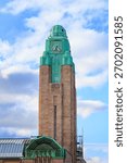 A close-up view of the iconic clock tower of Helsinki Central Railway Station, featuring its distinctive green copper roof and stone facade, against a partly cloudy sky