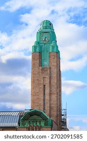 A close-up view of the iconic clock tower of Helsinki Central Railway Station, featuring its distinctive green copper roof and stone facade, against a partly cloudy sky