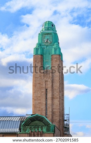 A close-up view of the iconic clock tower of Helsinki Central Railway Station, featuring its distinctive green copper roof and stone facade, against a partly cloudy sky