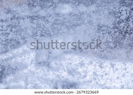 Close-up view of an icy window surface showcasing intricate frost patterns and frozen water droplets, reflecting the cold weather and seasonal changes
