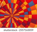 A close-up view inside a hot air balloon reveals vibrant shades of yellow, orange, red, maroon, and blue, creating a mesmerizing kaleidoscope of colors as light filters through the fabric.