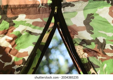 Close-up view of the inside from an open tent. Camping in nature. Camouflage background. Black mesh, lock, zipper, mosquito net. Brown, green, gray military khaki backdrop. Trekking.