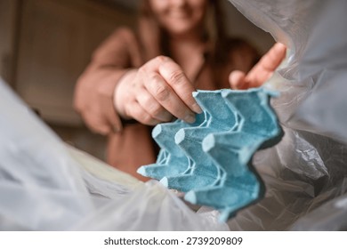 Close-up view from inside a trash bag of a woman throwing an empty egg carton into a recycling bag. Collecting packaging paper for recycling in bin POV. Waste segregation, waste sorting, waste recycle.