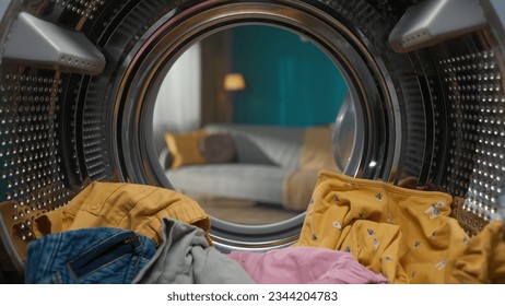 Closeup view from inside the washing machine, full of colorful clothes inside and opened door