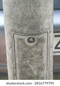 Close-up view of an inspection hatch with a triangular safety bolt on a weathered concrete street light pole.
