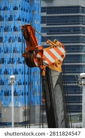 Close-up view of a large construction crane's lifting mechanism and boom, set against a backdrop of contemporary urban architecture