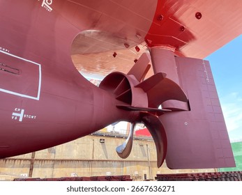 Close-up view of a large container ship propeller with installed twisted flipper and rudder in dry dock during maintenance.