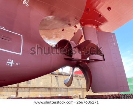 Close-up view of a large container ship propeller with installed twisted flipper and rudder in dry dock during maintenance.