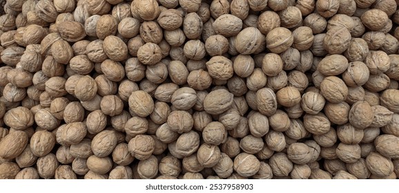 A close-up view of a large pile of unshelled walnuts, showcasing their natural, rough, and textured brown shells. the walnuts are arranged in a dense formation, emphasizing their earthy tones and org - Powered by Shutterstock