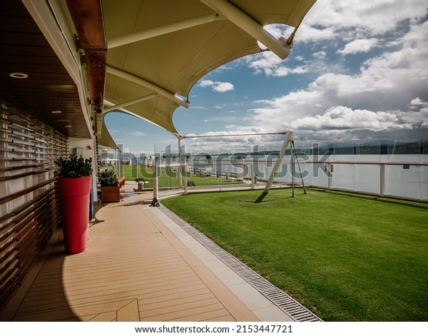 A closeup view of\
lawn grass area on upper deck of cruise vessel surrounded by glass\
panels and calm sea