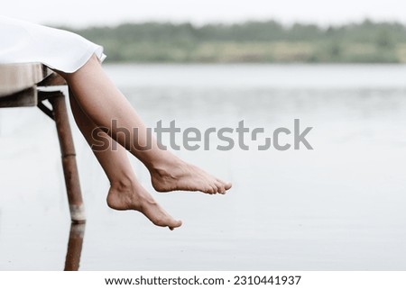 closeup view of legs, young beautiful caucasian woman in short white dress sits at wooden pier on river bank in summer, feet dangled in water, green trees in background, melancholy concept, copy space Foto d'archivio © 