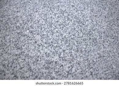 Close-up view of a light snow dusting on a speckled granite surface, showing winter texture, subtle contrast and a neutral monochrome background ideal for seasonal and abstract designs.