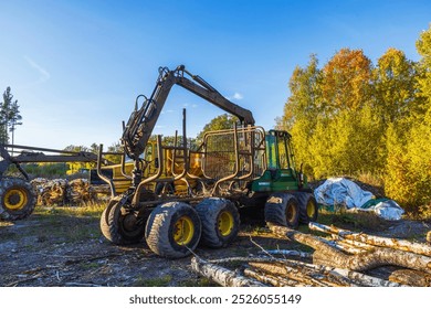 Close-up view of logging machine parked in forest area with logs stacked nearby during autumn. Sweden.