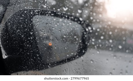 Close-up view looking through a dark car side mirror covered in heavy raindrops during a storm. Water splashes blur the bright window backdrop view entirely.
