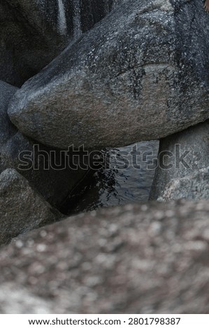 Close-up view looking through a narrow gap between large granite boulders down to the sea water below