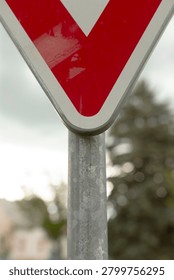 Close-up view of the lower portion of a triangular red and white yield traffic sign mounted on a weathered galvanized metal post. Shallow depth of field