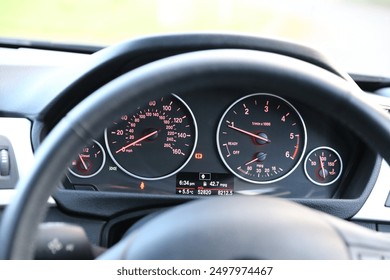 A close-up view of a luxury car interior, focusing on the steering wheel and the dashboard behind it. The steering wheel, wrapped in premium leather, features a minimalist design with functional butto - Powered by Shutterstock