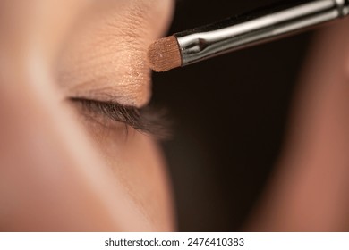 Close-up view of a makeup brush applying shimmery eyeshadow on a woman's closed eyelid. The detailed shot highlights the precision and care in the makeup application process - Powered by Shutterstock