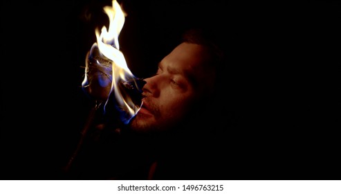 closeup view of male face illuminating two flaming torches in darkness, he is watching flame