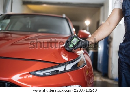 Closeup view of male hand, using film coating thickness gauge device to check car paint. Auto coating quality control.