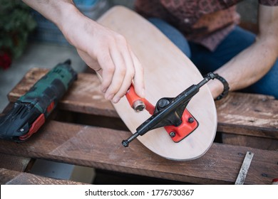 Close-up view of male hands assembling trucks on skateboard deck. Cropped man putting trucks on deck for making skateboard on wooden table. - Powered by Shutterstock