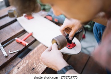 Close-up view of male hands fitting wheel to skateboard. Man's hands placing wheel to wooden skateboard on table with parts. - Powered by Shutterstock