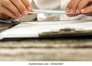 Closeup View Of Male Hands Holding Pencil Over Paperwork On Clipboard As Man Reads Through Terms And Conditions. Conceptual Of Signing Business Contract, Membership Or Legal Document.