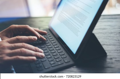 Closeup view of male hands typing electronic tablet keyboard-dock station.Businessman working at the wooden table.Horizontal, blurred background - Shutterstock ID 720823129