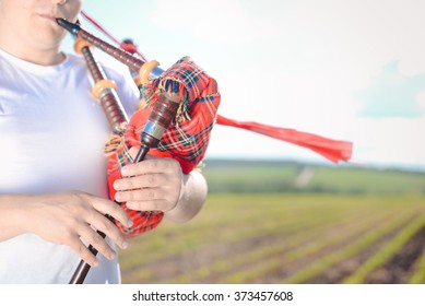 Closeup View Of Man Enjoying Playing Pipes In Scotish Traditional Kilt On Green Outdoors Summer Field Background