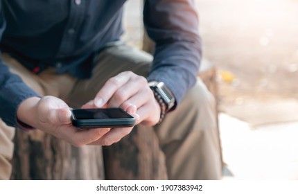Closeup view of man hands using smartphone while sitting outdoors.