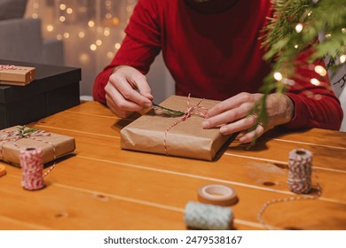 Close-up view of man wrapping Christmas present at home with blurred lights on the background - Powered by Shutterstock