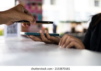 Close-up View Of A Man's Hand Scanning A QR Code With A Mobile Phone To Pay A Coffee Shopkeeper Who Is Holding Another Phone On The Counter.