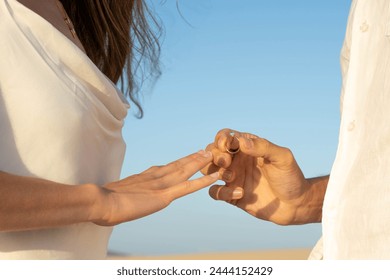 Close-up view of a marriage proposal with hands exchanging a wedding ring on a beach at sunset - Powered by Shutterstock