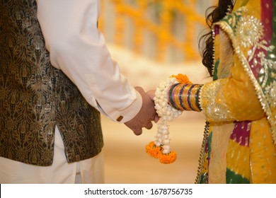 Closeup view of married couple holding hands, bangles of Indian bride, henna on hands, Yellow Garland