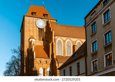 Close-up view of the massive brick tower and clock face of the Cathedral of SS. John the Baptist and John the Evangelist in Torun, Poland, set against a clear blue sky