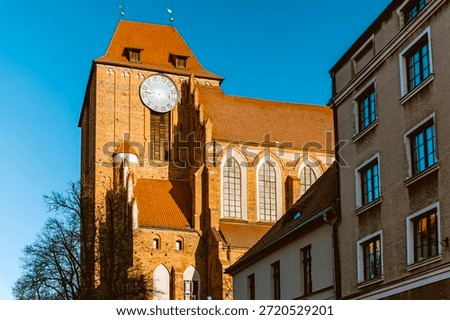 Close-up view of the massive brick tower and clock face of the Cathedral of SS. John the Baptist and John the Evangelist in Torun, Poland, set against a clear blue sky